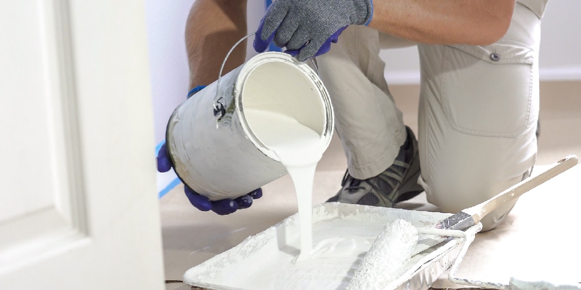 Photo of person inside a home pouring paint from a paint can into a tray.