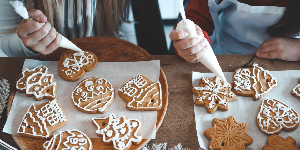 Photo of two sets of hands decorating holiday cookies.