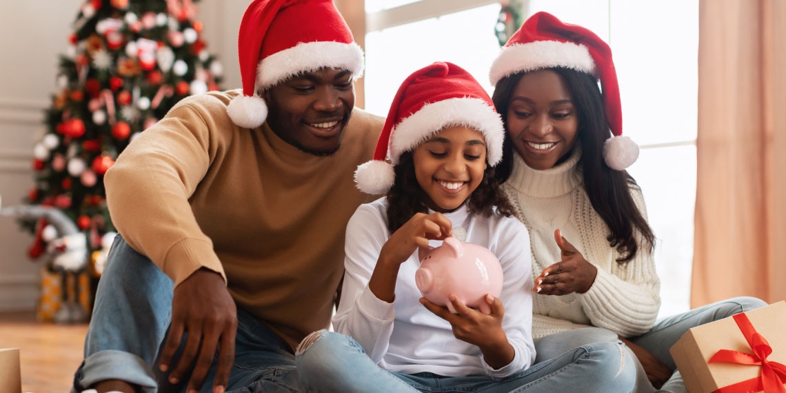 Photo of family hearing holiday hats with young girl putting money in piggy bank.