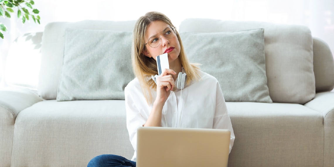 Photo of a woman thinking as she holds a credit card close to her face.