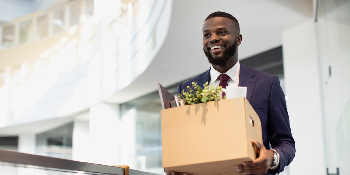 Photo of African American man smiling and carrying a box as he walks into his new job.