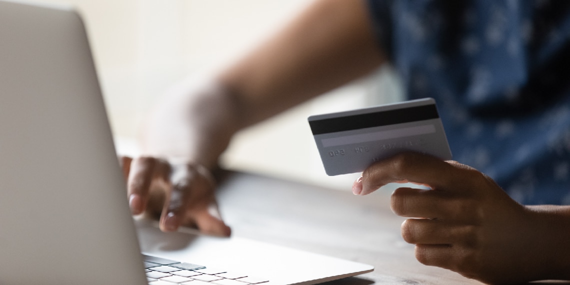 Photo of person holding up credit card while looking at a computer.