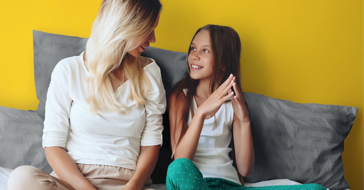 A mother turns to talk to her daughter who looks up to her and smiles.