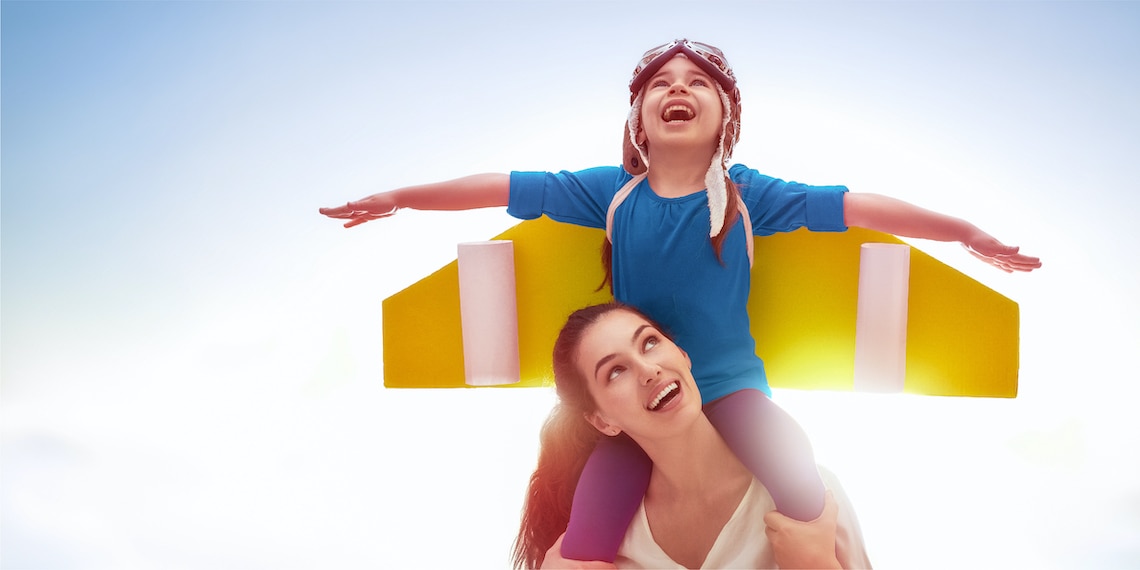 Child on mom’s shoulders with his hands out as if he’s trying to fly.