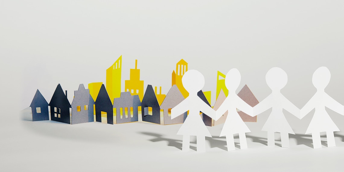 Paper doll cut outs holding hands in front of a paper village