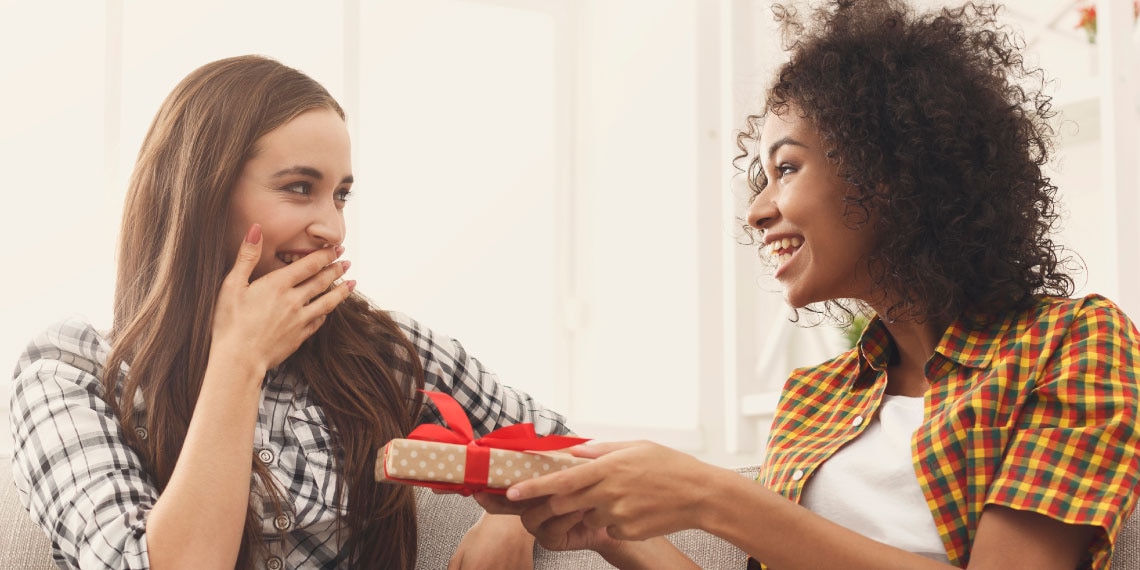 Photo of a woman giving another woman a wrapped gift.