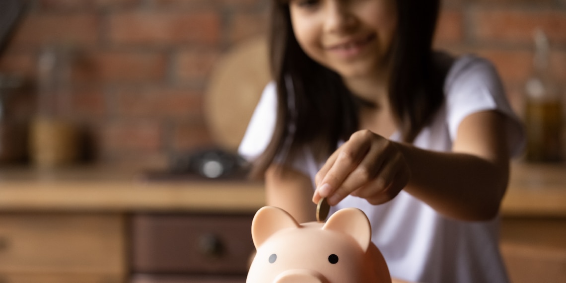 Photo of girl dropping savings into a piggy bank.