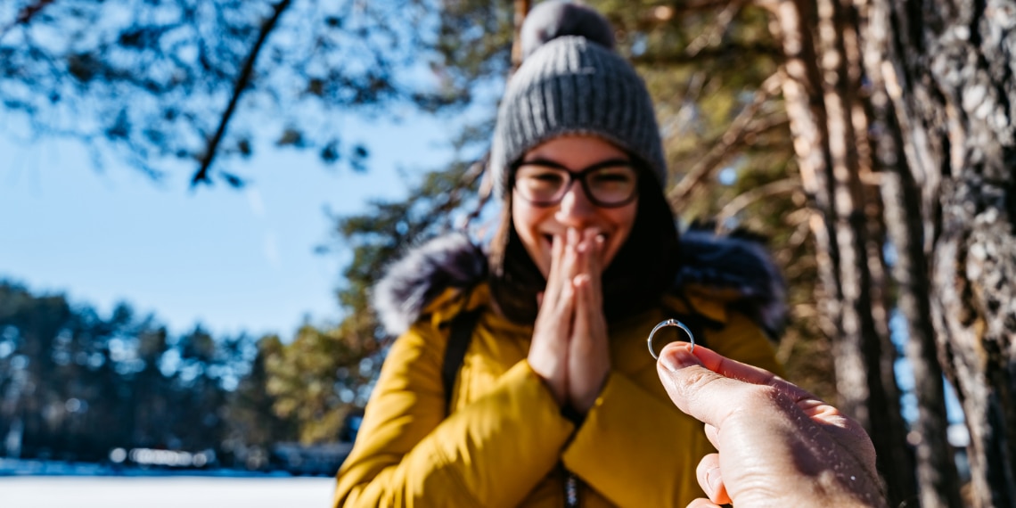 Photo of a woman in wintery woods gasping in surprise as she is being proposed to.